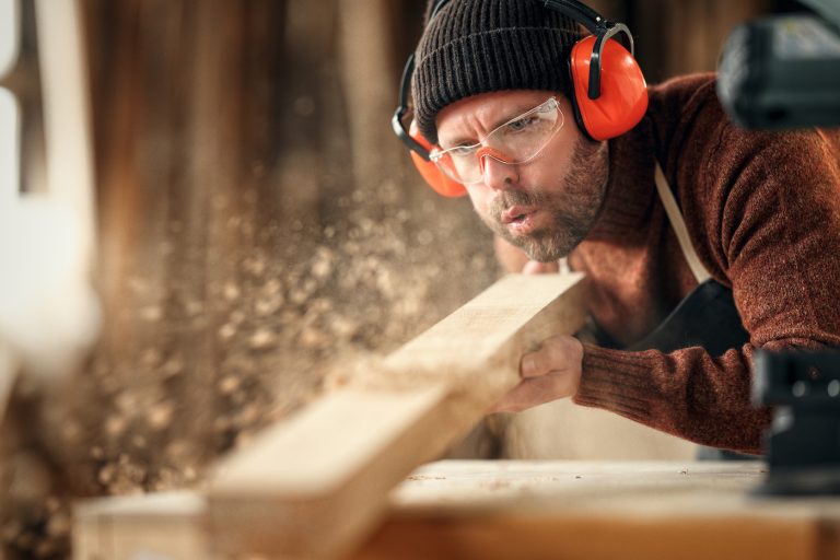 Carpenter blowing sawdust from wooden plank